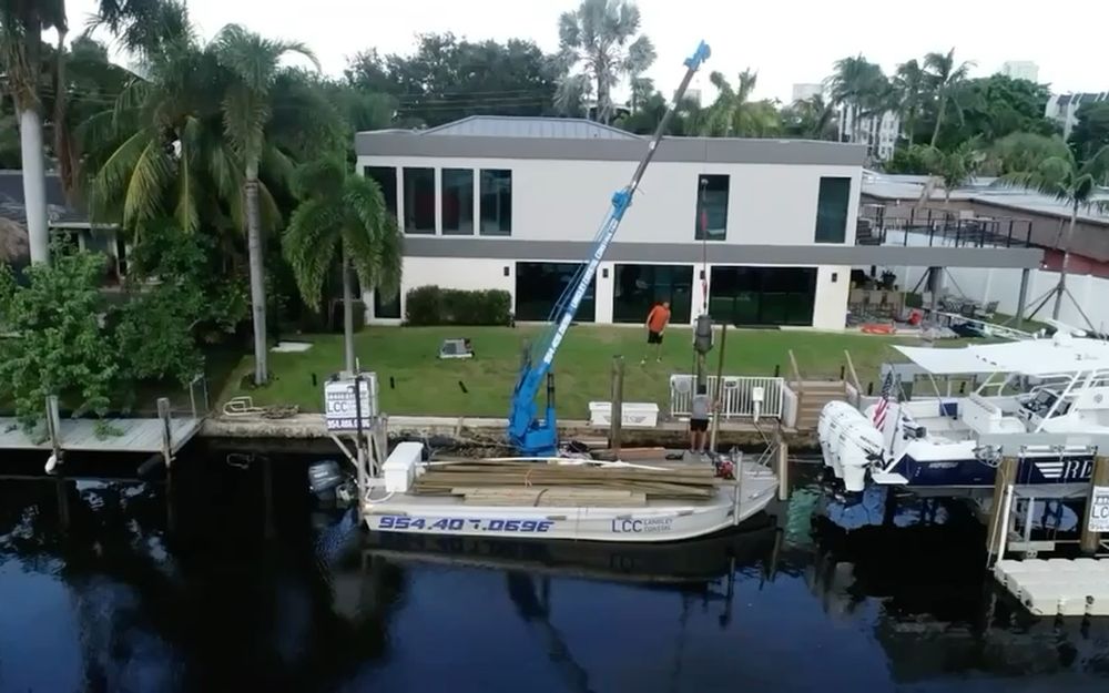 A crane barge working at a South Florida waterfront home, boat lifts along the dock