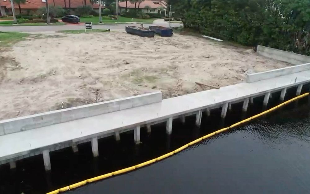 A new concrete seawall under construction on a South Florida canal, with a turbidity boom in the water